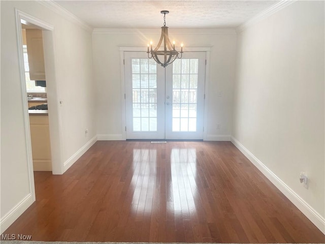 empty room with dark hardwood / wood-style floors, ornamental molding, french doors, and a chandelier