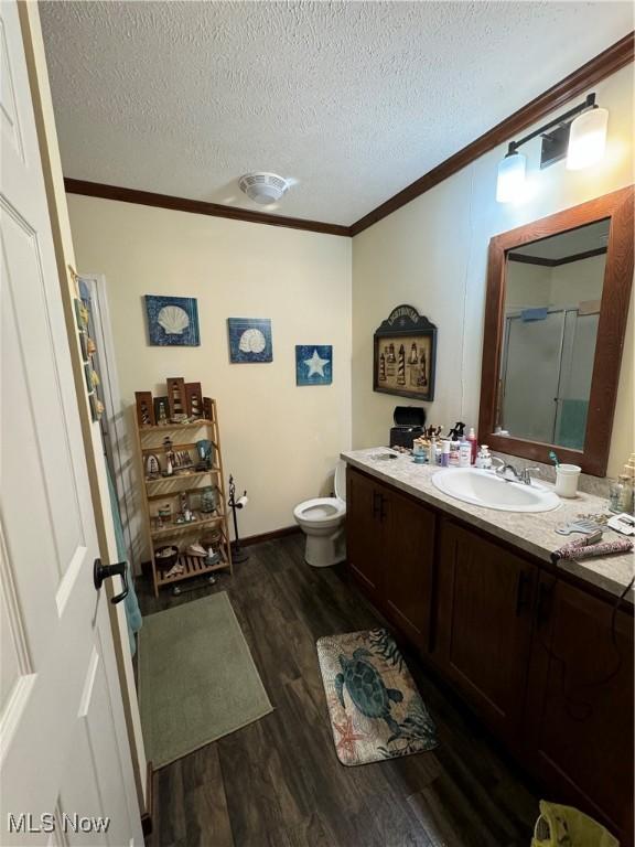 bathroom with walk in shower, wood-type flooring, a textured ceiling, vanity, and ornamental molding