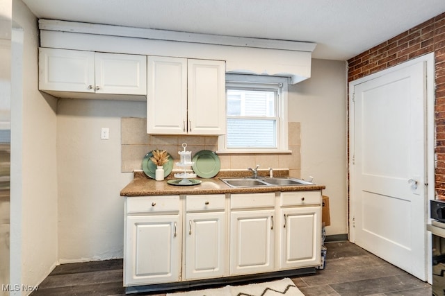 kitchen with backsplash, white cabinetry, sink, and brick wall