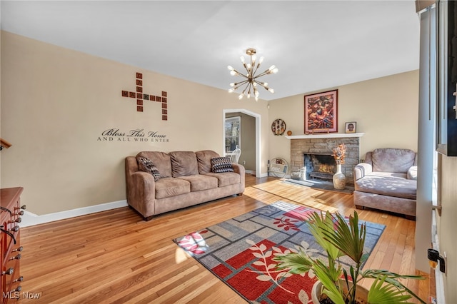 living room with a stone fireplace, hardwood / wood-style flooring, and a notable chandelier