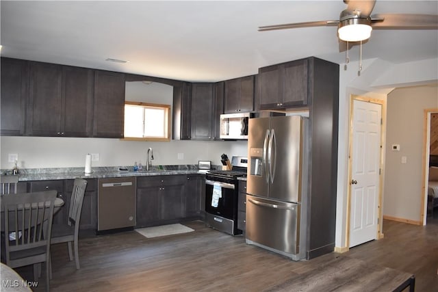 kitchen with dark wood-type flooring, sink, appliances with stainless steel finishes, stone countertops, and dark brown cabinetry