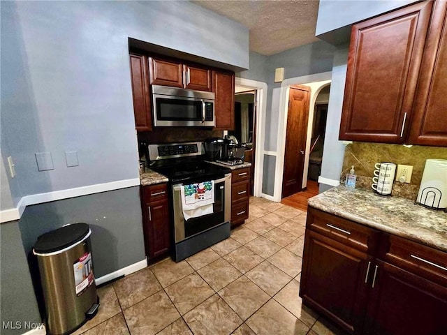 kitchen featuring light stone countertops, appliances with stainless steel finishes, backsplash, and light tile patterned flooring