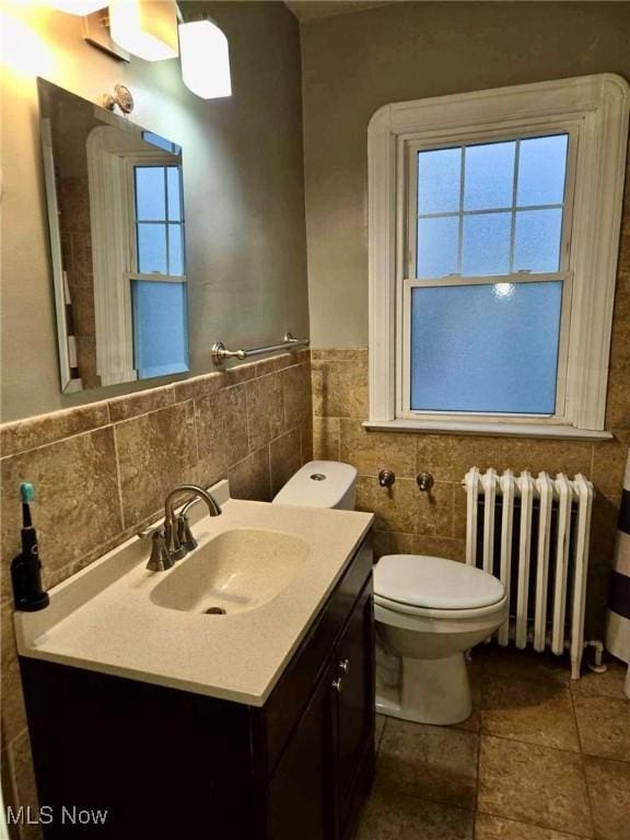 bathroom with radiator heating unit, vanity, tile walls, and toilet