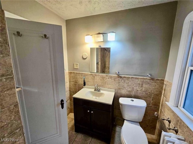 bathroom with vanity, lofted ceiling, toilet, a textured ceiling, and tile walls