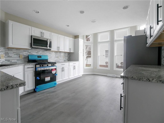 kitchen featuring white cabinets, range, decorative backsplash, and dark stone counters