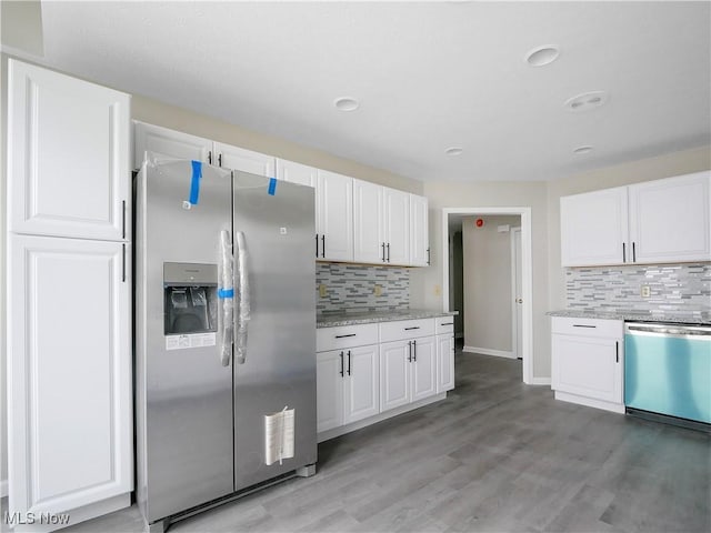 kitchen featuring white cabinets, appliances with stainless steel finishes, decorative backsplash, and light stone countertops