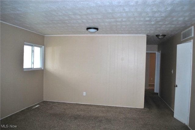 unfurnished room featuring a textured ceiling, dark carpet, and wooden walls