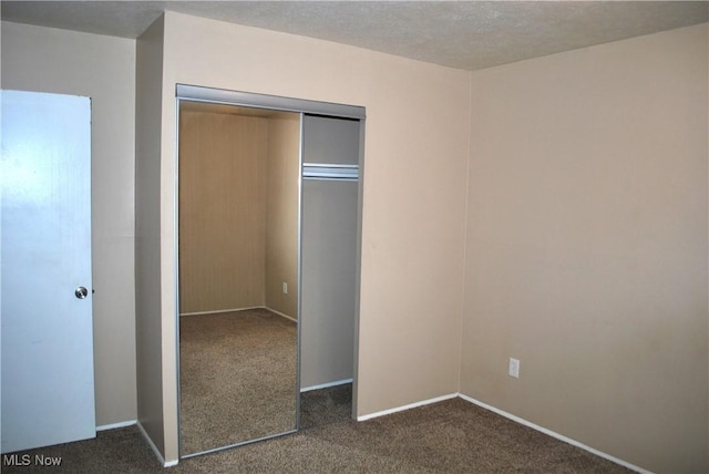 unfurnished bedroom featuring a closet, a textured ceiling, and dark colored carpet