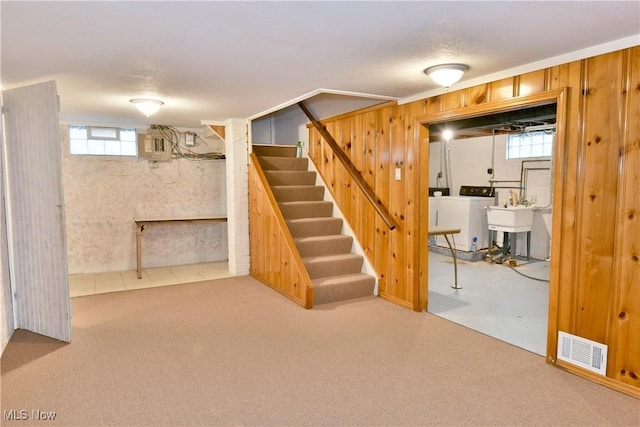 basement with washing machine and dryer, a wealth of natural light, wooden walls, and sink