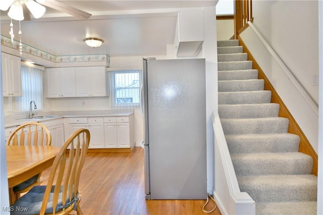 kitchen featuring white cabinets, light wood-type flooring, stainless steel refrigerator, and sink