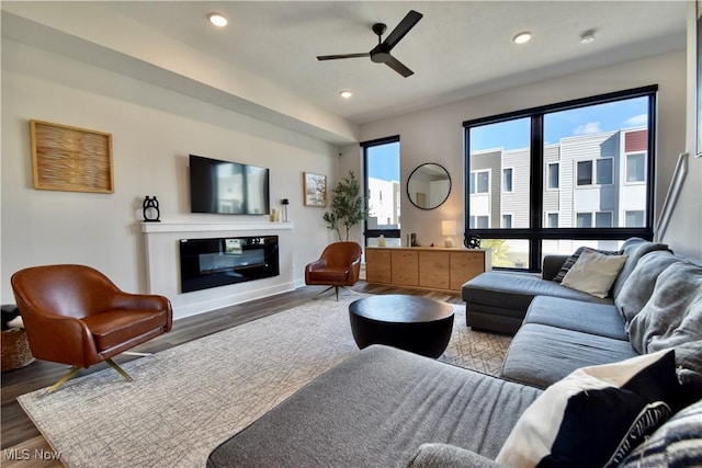 living room with baseboards, recessed lighting, a glass covered fireplace, a ceiling fan, and wood finished floors