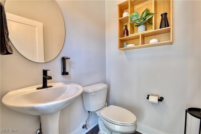 half bath with toilet, baseboards, and a sink