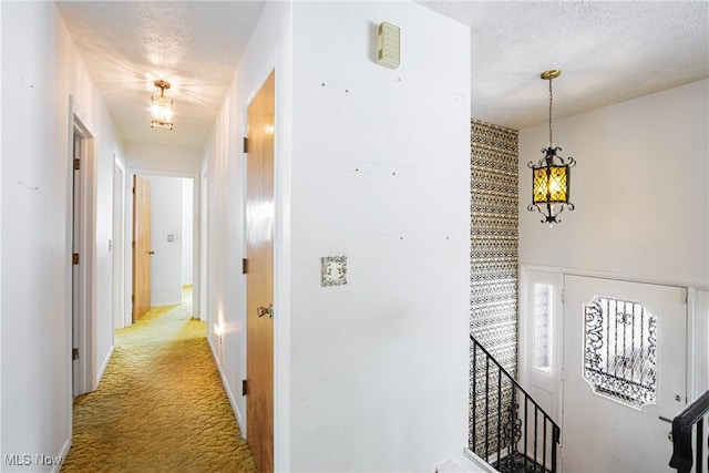 hallway with a textured ceiling and light colored carpet