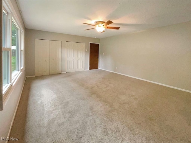 unfurnished bedroom featuring carpet flooring, two closets, and ceiling fan