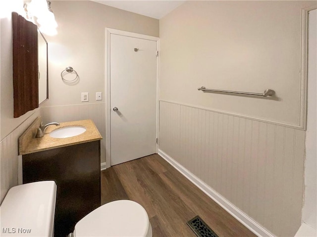 bathroom featuring wood walls, hardwood / wood-style floors, vanity, and toilet