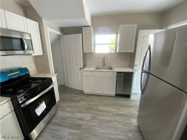 kitchen featuring sink, stainless steel appliances, backsplash, light hardwood / wood-style floors, and white cabinets