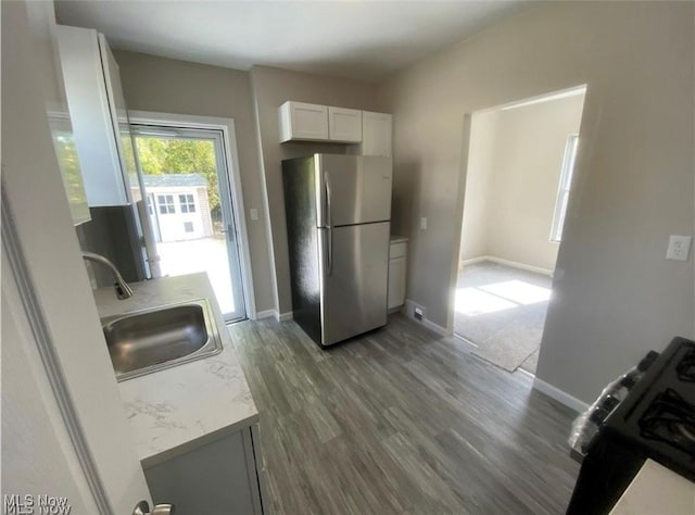 kitchen with sink, black stove, dark hardwood / wood-style flooring, stainless steel fridge, and white cabinets