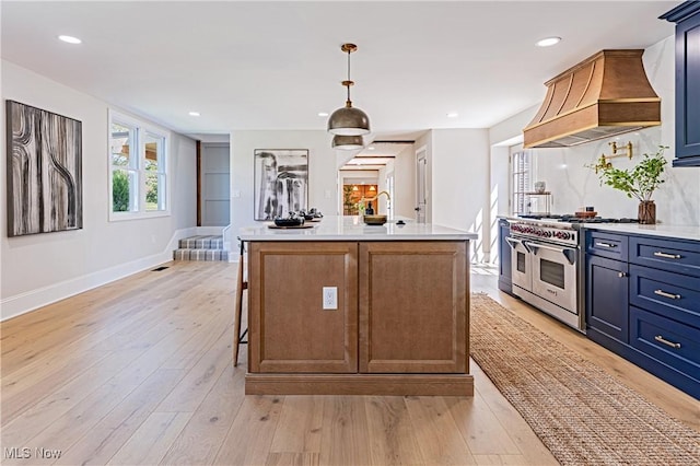 kitchen featuring hanging light fixtures, light hardwood / wood-style flooring, premium range hood, double oven range, and a center island with sink