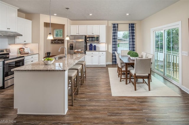 kitchen with appliances with stainless steel finishes, a center island with sink, white cabinetry, and hanging light fixtures