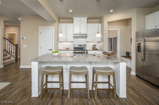 kitchen featuring a center island with sink, decorative light fixtures, white cabinetry, and appliances with stainless steel finishes