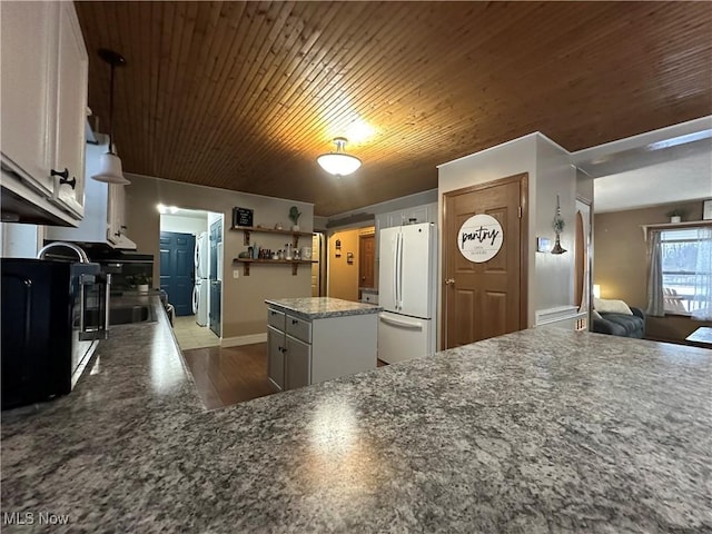 kitchen featuring light wood-type flooring, a kitchen island, white refrigerator, dark stone countertops, and white cabinetry