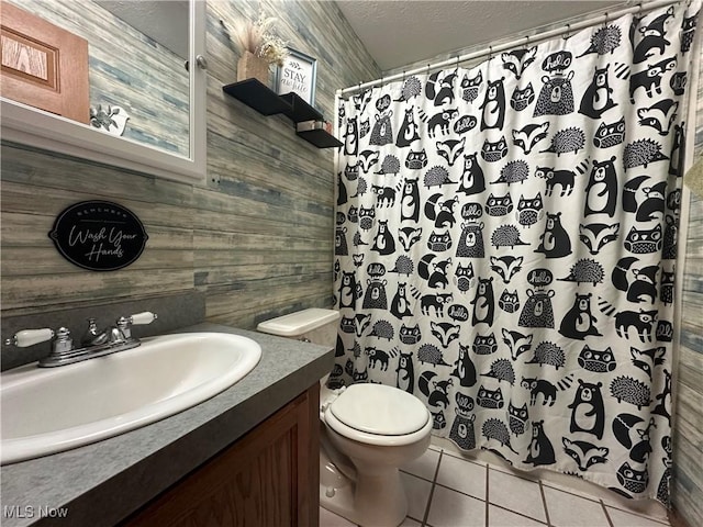 bathroom with vanity, wooden walls, tile patterned flooring, toilet, and a textured ceiling