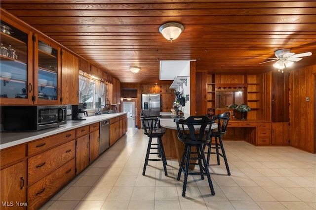 kitchen with a breakfast bar, wood walls, wooden ceiling, ceiling fan, and stainless steel appliances