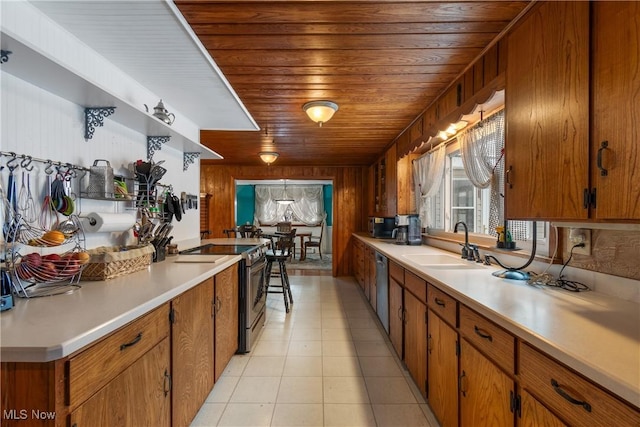 kitchen with sink, stainless steel appliances, wooden walls, light tile patterned floors, and wood ceiling