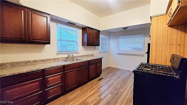 kitchen featuring black range oven, light stone counters, sink, and light hardwood / wood-style flooring