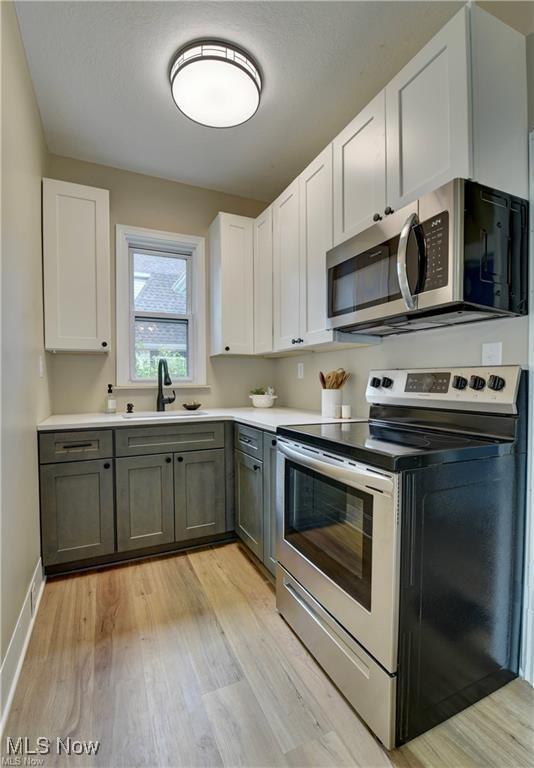 kitchen featuring sink, gray cabinets, light hardwood / wood-style floors, white cabinetry, and stainless steel appliances