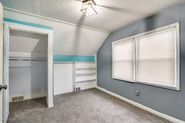 unfurnished bedroom featuring carpet floors, lofted ceiling, a textured ceiling, and a closet