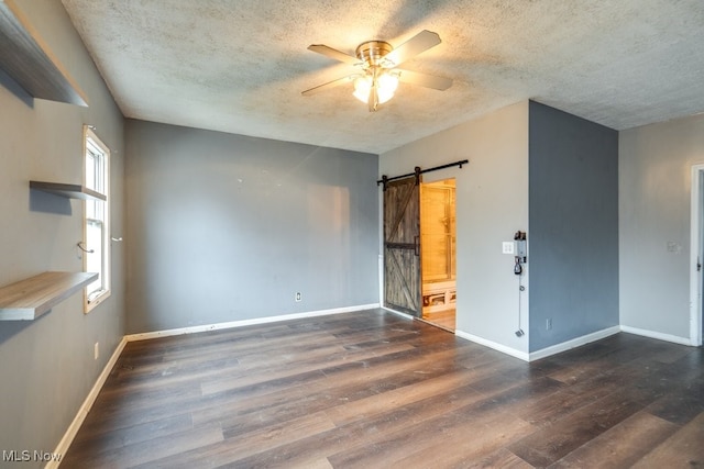 spare room featuring a textured ceiling, ceiling fan, a barn door, and dark hardwood / wood-style floors