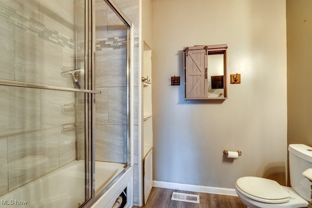 bathroom with hardwood / wood-style flooring, toilet, and bath / shower combo with glass door