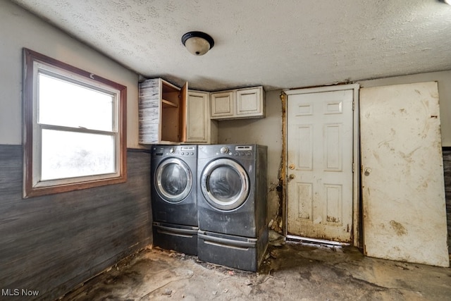 clothes washing area featuring washing machine and clothes dryer, wood walls, cabinets, and a textured ceiling