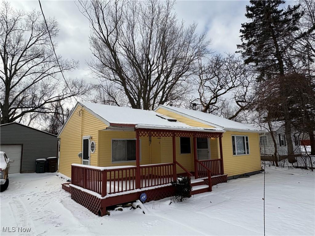 snow covered rear of property with an outbuilding, a porch, and a garage