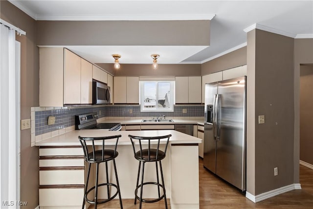 kitchen featuring sink, kitchen peninsula, crown molding, a kitchen bar, and appliances with stainless steel finishes