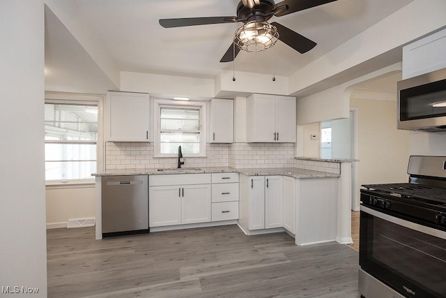 kitchen featuring white cabinets, sink, light stone countertops, appliances with stainless steel finishes, and light hardwood / wood-style floors