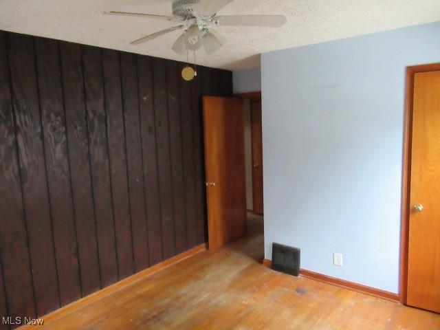 spare room featuring ceiling fan, light wood-type flooring, and wooden walls