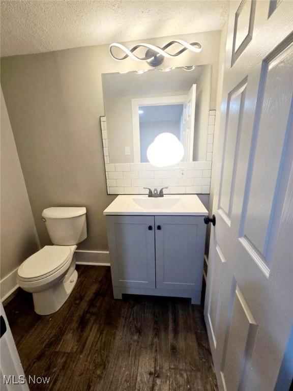 bathroom featuring hardwood / wood-style floors, vanity, decorative backsplash, toilet, and a textured ceiling