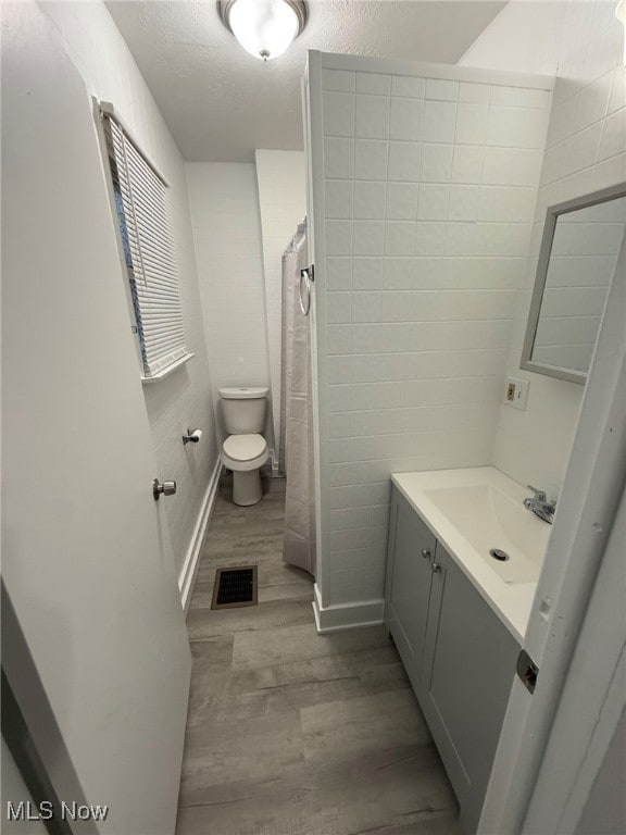 bathroom with a shower with curtain, vanity, a textured ceiling, wood-type flooring, and toilet