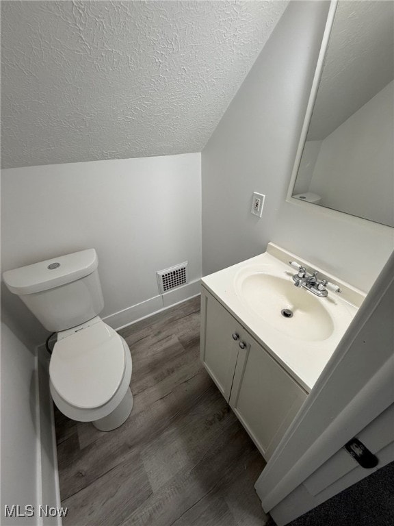 bathroom featuring a textured ceiling, vanity, vaulted ceiling, hardwood / wood-style flooring, and toilet