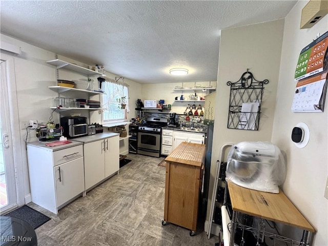 kitchen with butcher block countertops, white cabinetry, a textured ceiling, and stainless steel stove