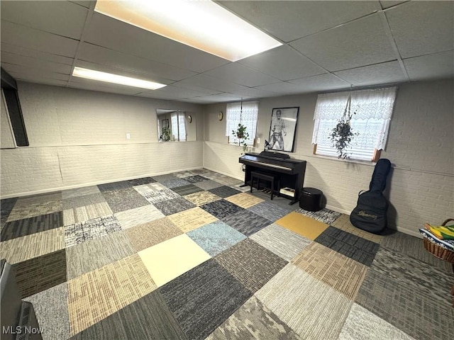 basement featuring a paneled ceiling, carpet floors, and brick wall