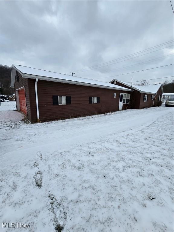 snow covered back of property featuring a garage