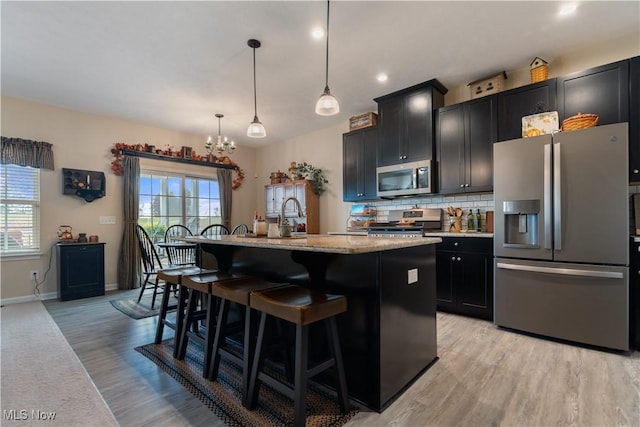 kitchen with a kitchen breakfast bar, stainless steel appliances, a center island with sink, light hardwood / wood-style floors, and hanging light fixtures