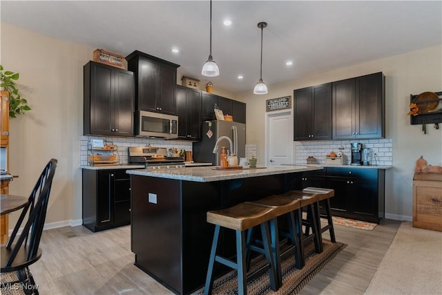 kitchen featuring pendant lighting, light wood-type flooring, stainless steel appliances, and a kitchen island with sink