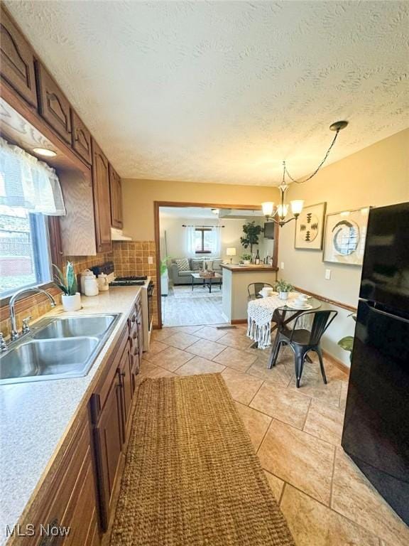 kitchen featuring sink, backsplash, pendant lighting, a textured ceiling, and black refrigerator