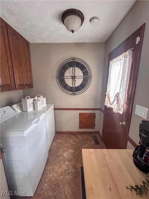 clothes washing area with cabinets, a textured ceiling, and independent washer and dryer