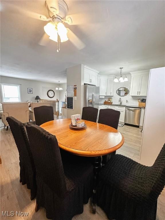 dining space with sink, ceiling fan with notable chandelier, and light wood-type flooring