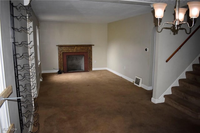 unfurnished living room with dark colored carpet, a fireplace, and a notable chandelier